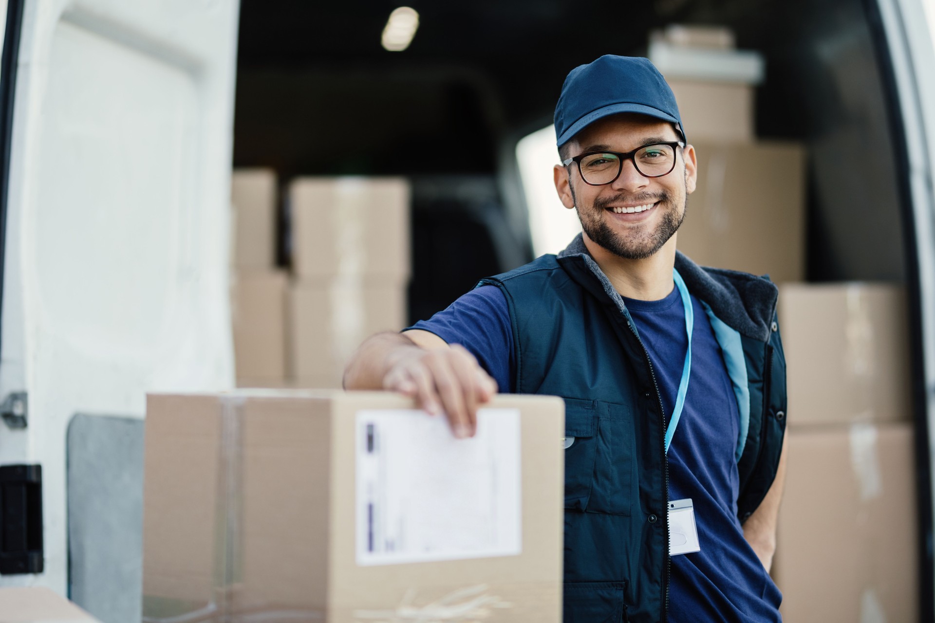 Young happy delivery man with cardboard boxes looking at camera.